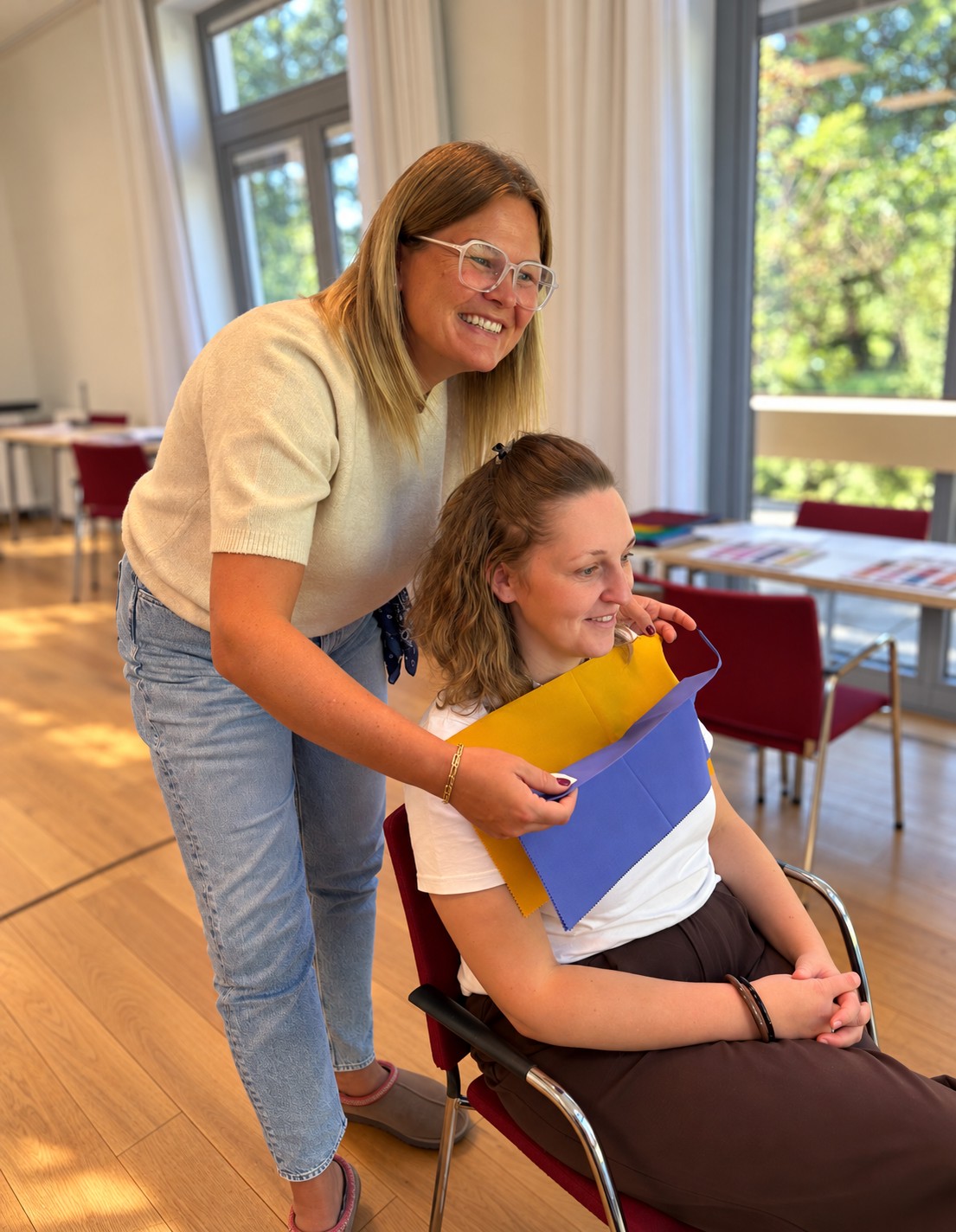 Ann-Christin legt einer Kundin gelbe und violette Farbtücher an, um ihre Farbwirkung zu vergleichen.